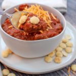 White bowl filled with chili and topped with cheese
