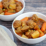 White bowl filled with meatballs, carrots, celery, potatoes and peas