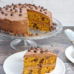 A Slice of cake on a white plate with the full cake in the background