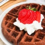 Brownie mix waffles with whipped cream and strawberries on top on a white plate