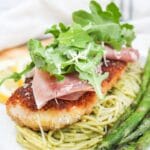 chicken bellagio over pasta topped with arugula and served wit asparagus.