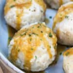 Round potato balls on a gray plate topped with pan gravy and chopped parsley.