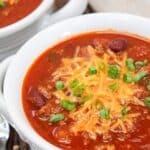 chili served in a white bowl. Topped with shredded cheddar cheese and sliced green onions.