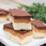 Cookie style bars cut into rectangles. The bars are layers wit h shortbread on the bottom, then caramel, and chocolate on top. The bars are stacked on top of each other.