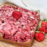 Cake resting on a wood cutting board with strawberries cooked into the top. Fresh strawberries for garnish.