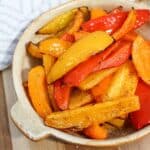 red, yellow, and orange sliced bell peppers cooked, charred, and served in a tan bowl.