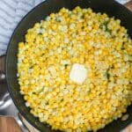 Cooked corn in black skillet with butter on top.