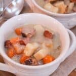 Chopped cooked carrots, onions, sausage, bratwurst, and potatoes in a creamy broth served in a white bowl.