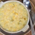 creamed corn with bits of chopped jalapenos in a brown bowl with a spoon on the side.
